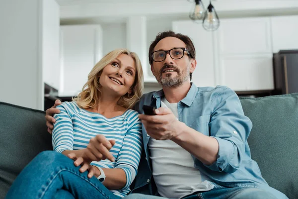 Enfoque selectivo de sonreír pareja madura viendo la televisión en el sofá - foto de stock