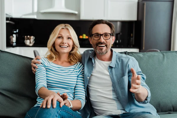 Enfoque selectivo del hombre guapo abrazando hermosa esposa sonriente en el sofá - foto de stock