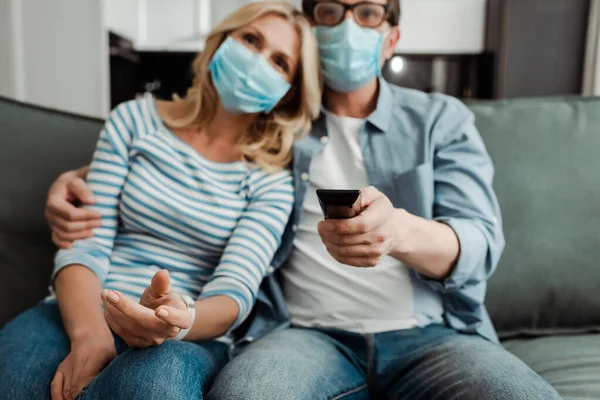 Selective focus of mature couple in medical masks watching tv at home — Stock Photo