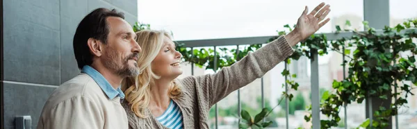 Panorama einer lächelnden Frau, die mit der Hand in die Nähe ihres Mannes auf der Terrasse zeigt — Stockfoto