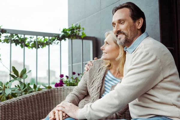 Mature homme étreignant belle femme souriante sur canapé sur la terrasse — Photo de stock