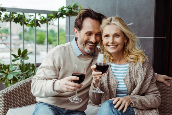 Sorrindo casal maduro segurando copos de vinho no sofá de vime no terraço — Fotografia de Stock