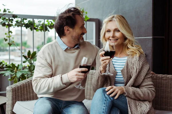 Hombre maduro guapo mirando sonriente esposa con copa de vino en la terraza - foto de stock