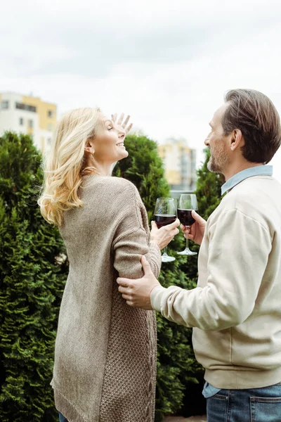 Smiling woman pointing with hand near husband with glass of wine on urban street — Stock Photo