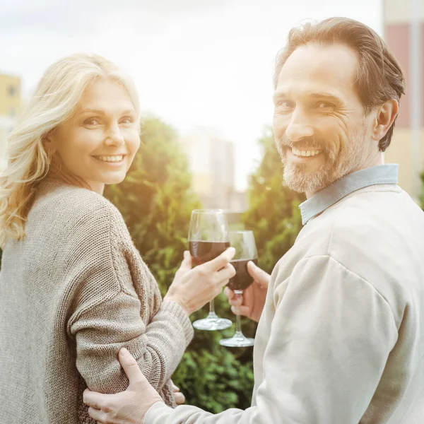 Toned image of smiling mature couple holding glasses of wine on urban street — Stock Photo