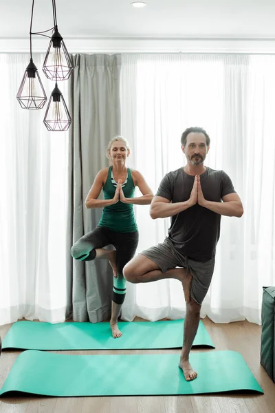 Pareja madura practicando yoga en colchonetas de fitness en casa - foto de stock