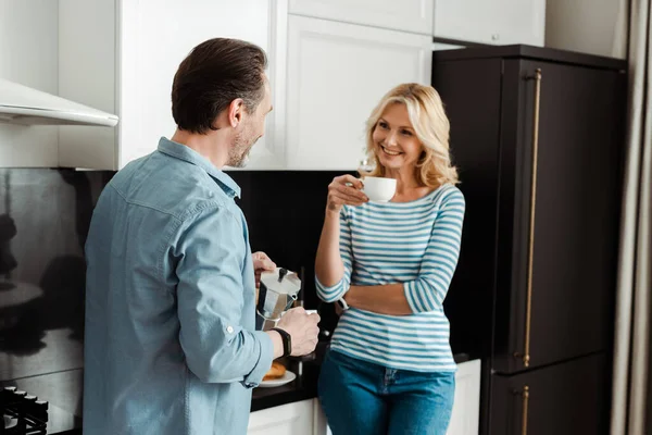 Hermosa mujer sonriendo al marido vertiendo café en la cocina — Stock Photo