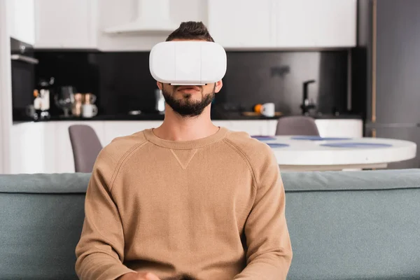 Bearded man in virtual reality headset sitting in living room — Stock Photo