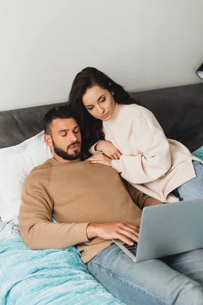 Bello freelance utilizzando laptop vicino bella fidanzata in camera da letto — Foto stock