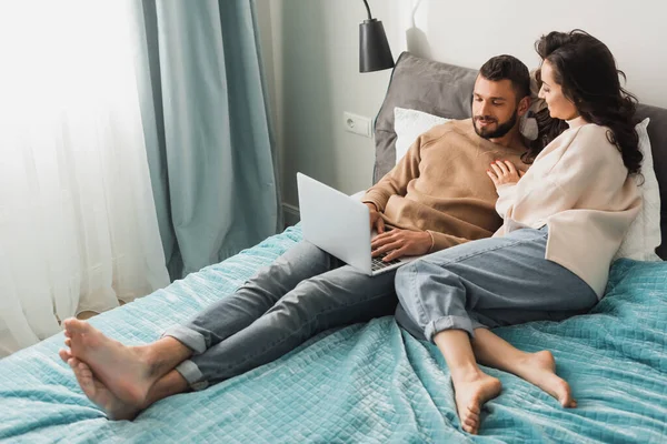 Happy freelancer using laptop near beautiful girlfriend in bedroom — Stock Photo