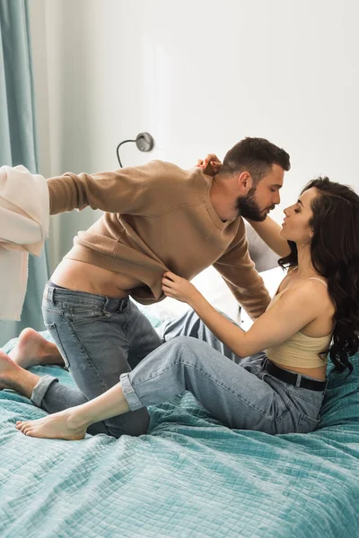 Side view of passionate man holding sweatshirt of girlfriend in bedroom — Stock Photo