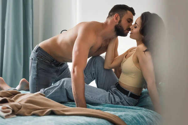 Vista lateral del hombre musculoso y hermosa mujer besándose en el dormitorio - foto de stock