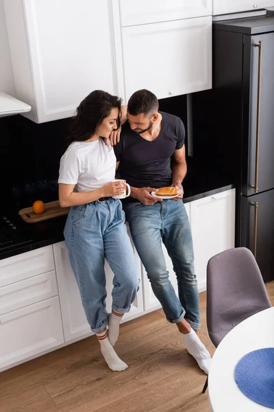 Vista de alto ângulo de menina feliz segurando copo e de pé com namorado na cozinha — Fotografia de Stock