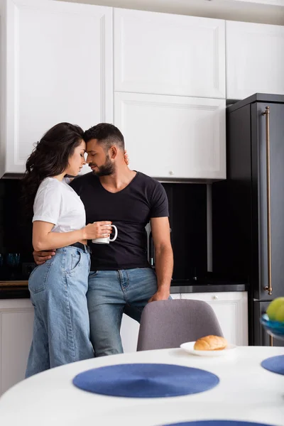 Messa a fuoco selettiva di bella ragazza in possesso di tazza e in piedi con il fidanzato in cucina — Foto stock