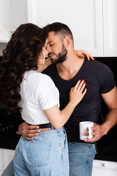 Joven mujer abrazando barbudo hombre con taza de café - foto de stock