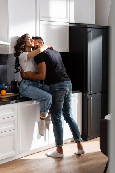 Barbudo hombre besos hermosa mujer con cerrado ojos en cocina - foto de stock