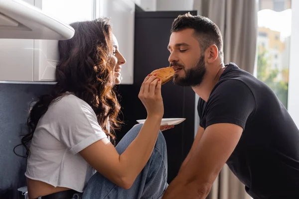 Selektiver Fokus glücklicher Mädchen, die ihren schönen Freund mit Croissant füttern — Stockfoto