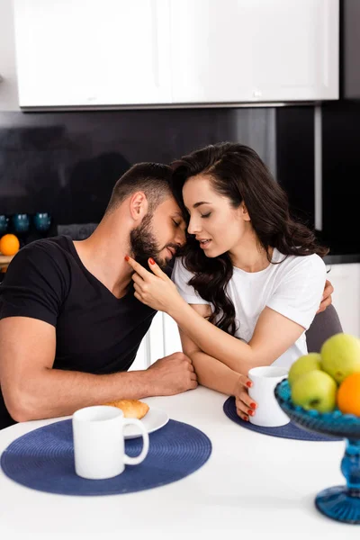 Selektiver Fokus der jungen Frau, die ihren hübschen Freund in der Nähe von Tassen und leckerem Frühstück auf dem Tisch berührt — Stockfoto