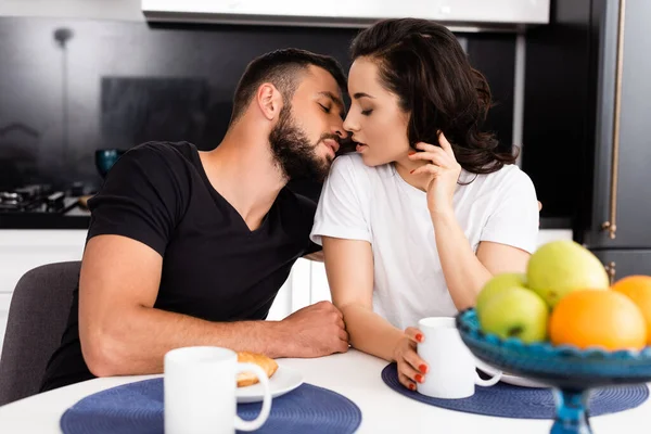 Enfoque selectivo de la mujer joven y guapo novio cerca de tazas y sabroso desayuno en la mesa - foto de stock