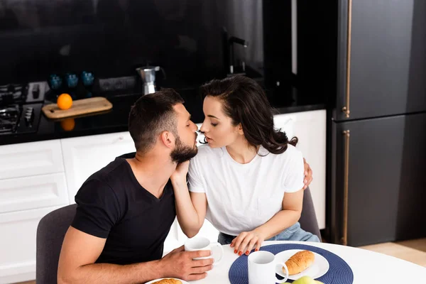 Jeune femme touchant beau petit ami près des tasses sur la table — Photo de stock