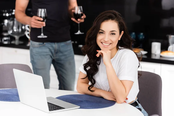 Foco seletivo de freelancer alegre sorrindo perto de namorado com copos de vinho — Fotografia de Stock