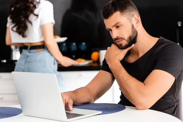 Selective focus of pensive freelancer using laptop near girlfriend in kitchen — Stock Photo