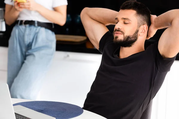 Enfoque selectivo de freelancer guapo mirando portátil cerca de novia en la cocina - foto de stock