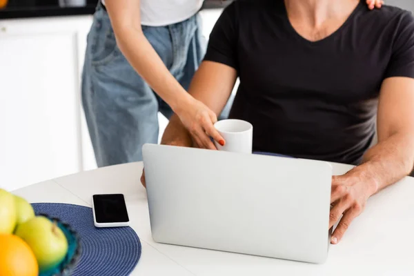 Ausgeschnittene Ansicht einer Frau, die Tasse in der Nähe ihres Freundes berührt, Laptop und Smartphone mit leerem Bildschirm — Stockfoto