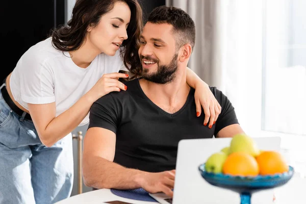 Foco seletivo de mulher bonita abraçando namorado feliz perto do laptop — Fotografia de Stock