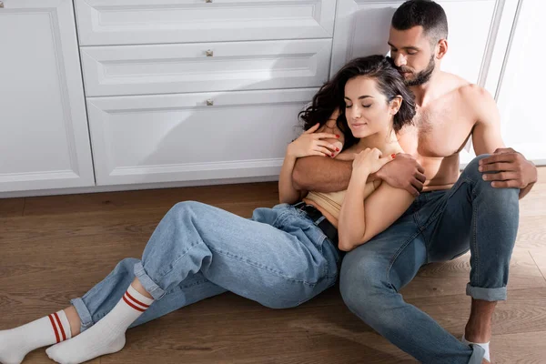 Muscular man hugging beautiful girl while sitting on floor — Stock Photo