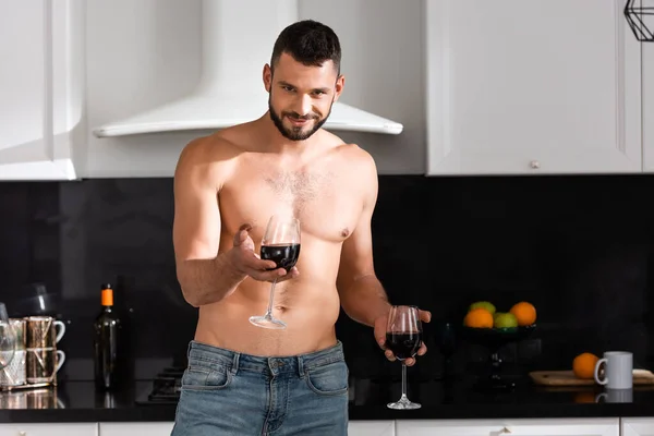 Hombre feliz y musculoso sosteniendo vasos con vino tinto - foto de stock