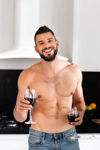 Homme heureux et torse nu tenant des verres avec du vin rouge — Photo de stock