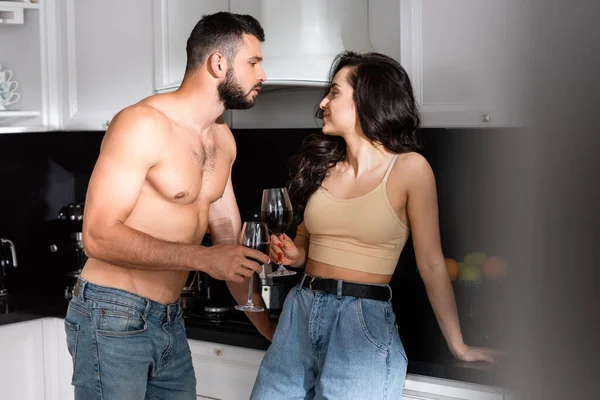 Selective focus of shirtless man and happy woman holding glasses of red wine and looking at each other — Stock Photo