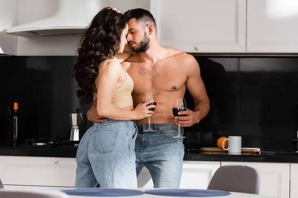 Enfoque selectivo de la mujer joven sosteniendo copa de vino tinto y mirando al hombre sin camisa - foto de stock