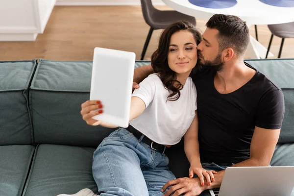 Messa a fuoco selettiva di barbuto freelance baciare guancia di ragazza prendendo selfie mentre tenendo tablet digitale — Foto stock
