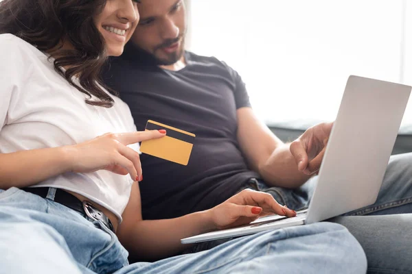 Enfoque selectivo de la mujer feliz celebración de la tarjeta de crédito cerca de novio barbudo y portátil - foto de stock