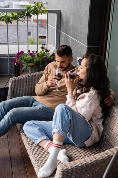 Schöner Mann und attraktive Frau sitzen auf dem Sofa im Freien und trinken Rotwein — Stockfoto