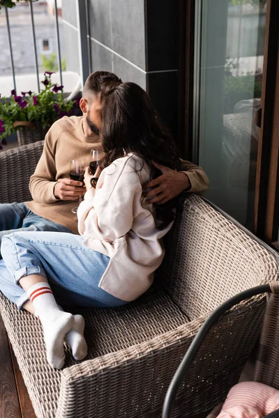 Paar sitzt auf Sofa im Freien und hält Weingläser, während es sich draußen küsst — Stockfoto