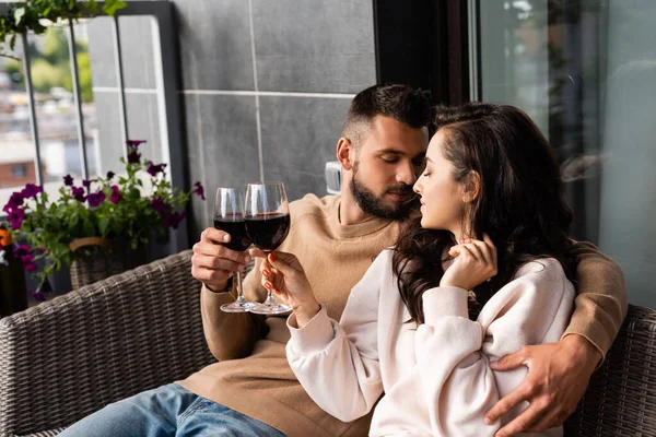 Bel homme étreignant belle femme et cliquetis verres de vin rouge à l'extérieur — Photo de stock