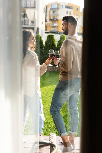 Selective focus of man and beautiful woman standing outside and clinking glasses of red wine — Stock Photo