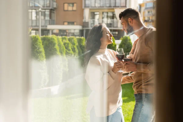 Селективное внимание красивого мужчины и красивой женщины, стоящих снаружи и звон бокалов красного вина — стоковое фото