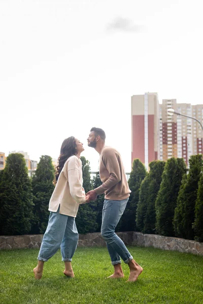 Vista lateral da mulher bonita e homem barbudo de mãos dadas enquanto em pé na grama verde — Fotografia de Stock
