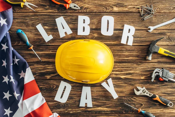 Top view of tools, safety helmet and american flag near labor day lettering on wooden surface — Stock Photo