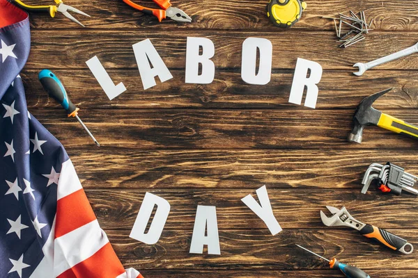 Top view of tools and american flag near labor day lettering on wooden surface — Stock Photo