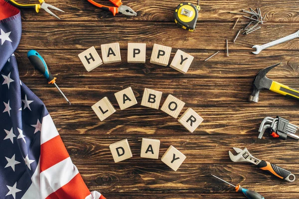 Vue du dessus des outils et drapeau américain près des cubes avec lettrage heureux de la journée de travail sur la surface en bois — Photo de stock