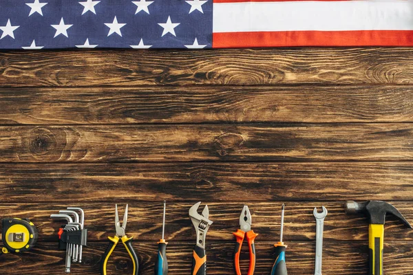 Вид зверху на металеві інструменти та американський прапор на дерев'яній поверхні, концепція робочого дня — стокове фото