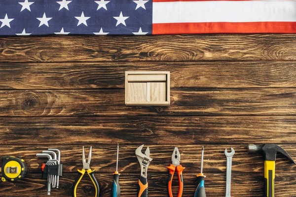 Вид зверху на металеві інструменти, коробка і американський прапор на дерев'яній поверхні, концепція робочого дня — стокове фото