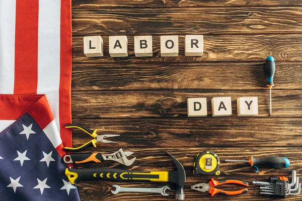 Top view of metallic tools and american flag near cubes with labor day lettering on wooden surface — Stock Photo