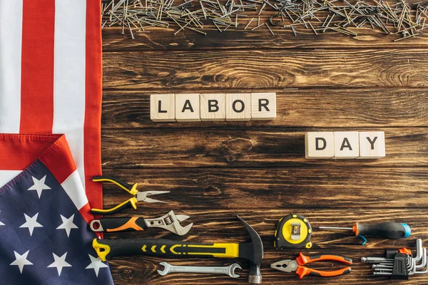 Top view of metallic instruments and nails near american flag and cubes with labor day lettering on wooden surface — Stock Photo