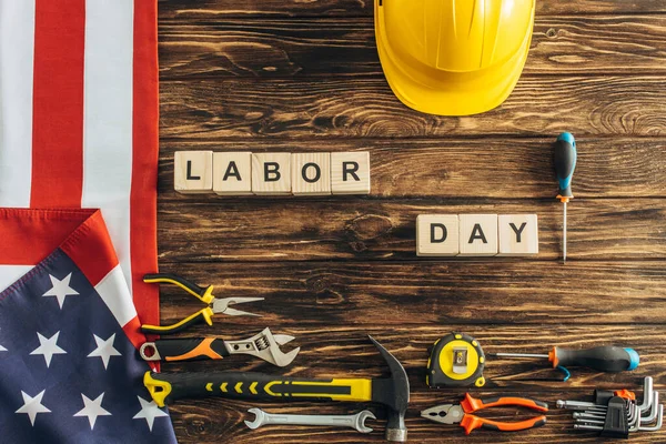 Top view of interments, safety helmet and american flag near cubes with labor day lettering on wooden surface — Stock Photo